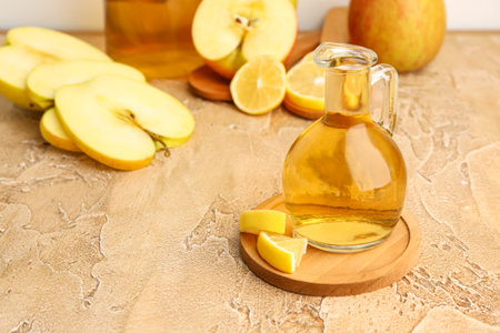 Jug of apple cider vinegar and fruits on color table