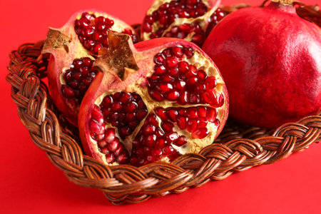 Wicker basket with fresh pomegranates on red background, closeupの写真素材