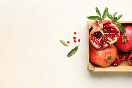 Wooden box with fresh pomegranates and plant branches on light backgroundの写真素材