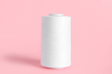 White thread spool on pink background
