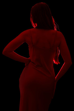 Silhouette of young woman in silky dress on black background, back viewの写真素材