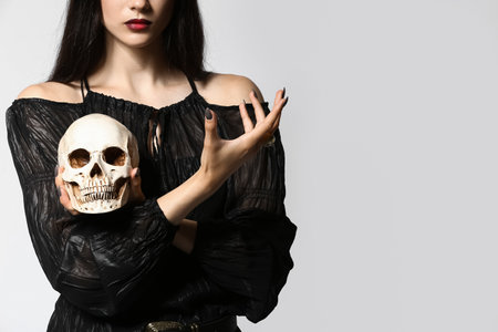 Young witch with human skull on light backgroundの写真素材