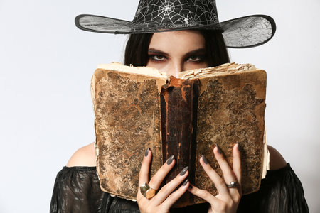 Young witch with spell book on light background