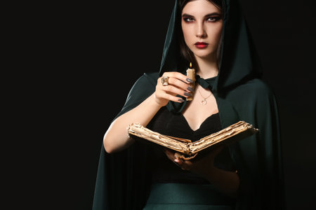 Young witch with spell book and candle on dark background