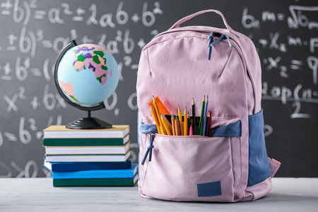 School backpack with stationery, books and globe on table in classroom