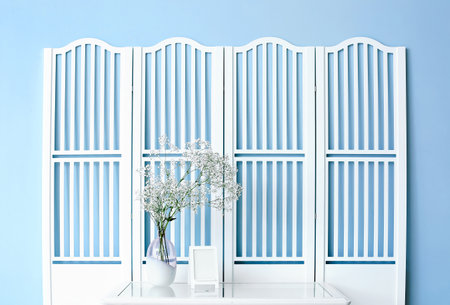 Vase with gypsophila flowers and frame on table near white folding screenの写真素材