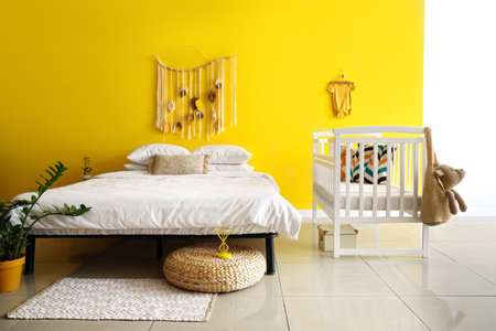 Big comfortable bed and white crib near yellow wallの写真素材