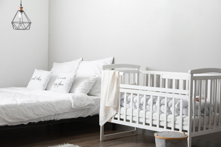 White crib and comfortable bed near light wallの写真素材