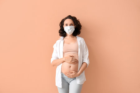 Young pregnant woman in medical mask on color backgroundの写真素材