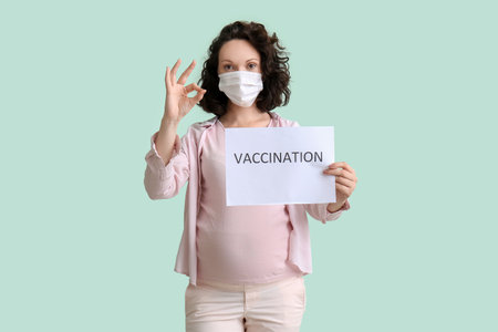 Young pregnant woman holding paper with word VACCINATION on color backgroundの写真素材