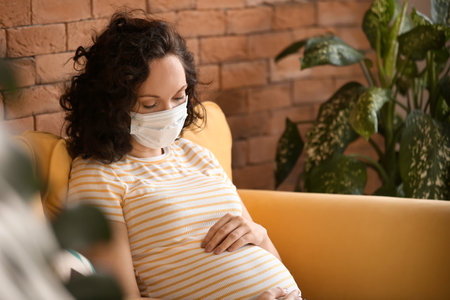 Young pregnant woman with medical mask at home
