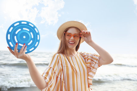 Happy young woman with flying disc on sea beachの写真素材