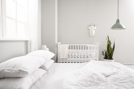 Big bed and comfortable baby crib in interior of cozy room