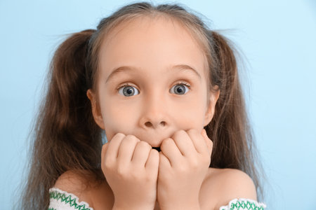 Portrait of surprised little girl with ponytails on blue background, closeupの写真素材