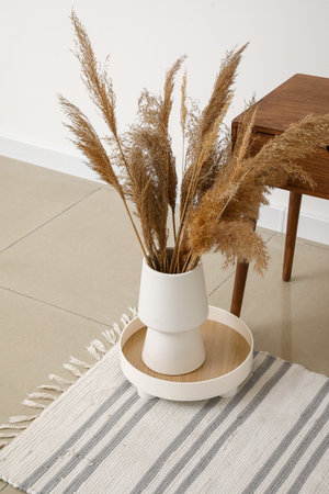 Vase with dry reeds on floor in room