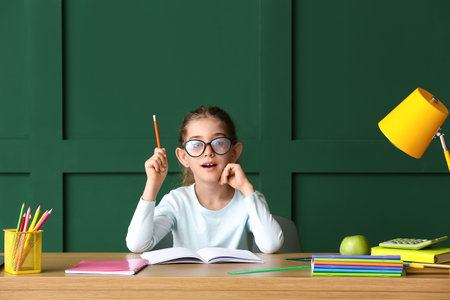 Little girl doing homework at table on color background