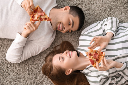 Happy young couple with slices of tasty pizza lying on carpet, top viewの写真素材
