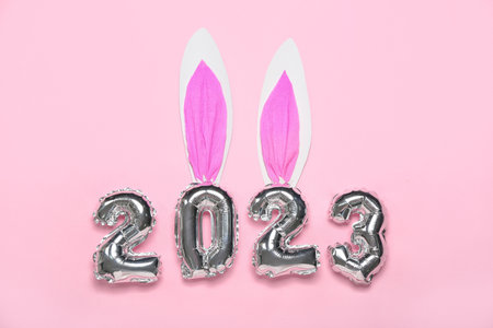 Figure 2023 made of balloons with paper bunny ears on pink background
