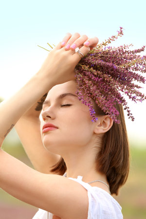Beautiful young woman with bouquet of summer flowers outdoorsの写真素材