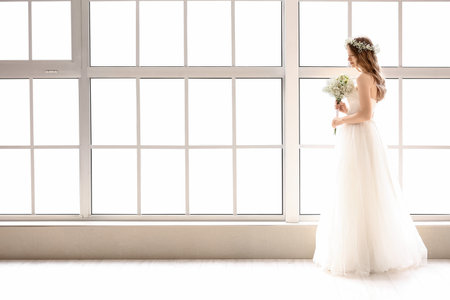 Beautiful bride with bouquet of flowers near windowの写真素材