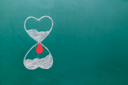 Drawing of heart shaped hourglass with red blood drop on green background. Donation conceptの写真素材