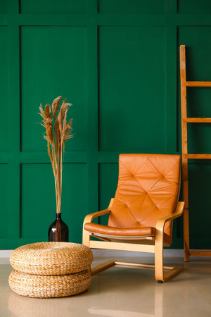 Vase with dry reeds, armchair, ladder and poufs near green wallの写真素材