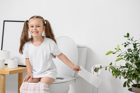 little girl sitting on toilet bowl in bathroomの写真素材