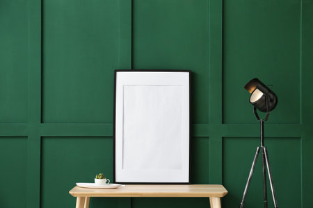 Wooden table with blank photo frame near green wall
