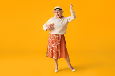 Mature woman with tasty popcorn on color backgroundの写真素材
