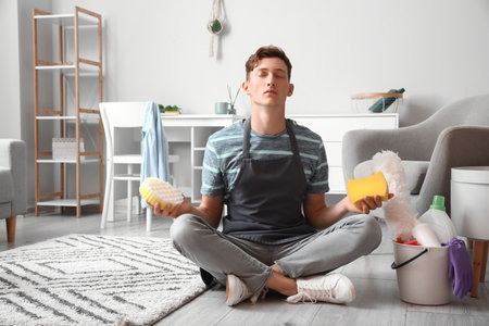 Handsome man with different cleaning sponges meditating at homeの写真素材