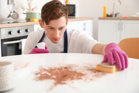 Young man cleaning dining table with sponge in kitchenの写真素材