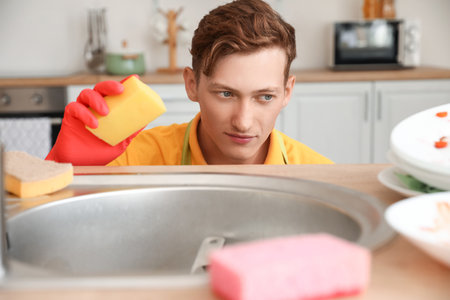 Young man with cleaning sponge in the kitchenの写真素材