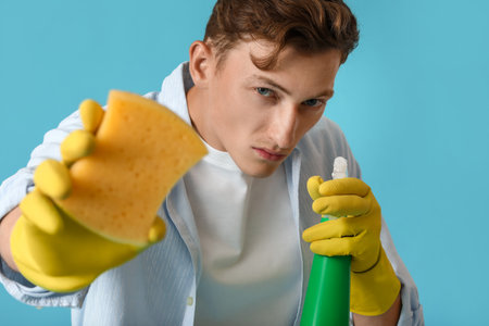 Handsome man with sponge and detergent on blue background, closeupの写真素材