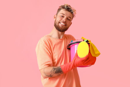 Handsome young man with cleaning supplies on pink backgroundの写真素材