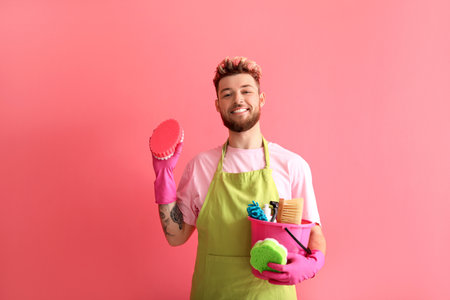 Handsome young man with cleaning supplies on pink backgroundの写真素材