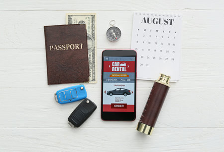 Mobile phone with open car rent app, passport, keys, spyglass and calendar on white wooden backgroundの写真素材