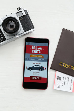 Mobile phone with open car rent app, passport and photo camera on white wooden backgroundの写真素材