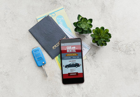 Mobile phone with open car rent app, passport, key and flowerpots on light background