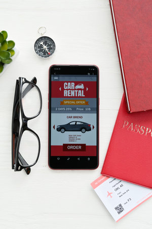 Mobile phone with open car rent app, passport, ticket and eyeglasses on white wooden backgroundの写真素材