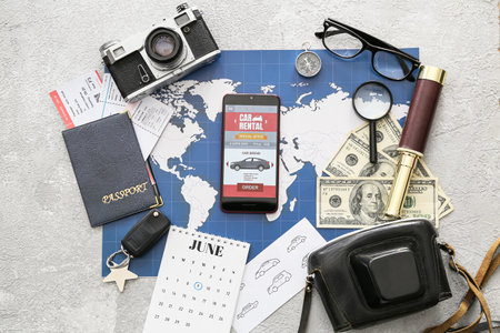 Mobile phone with open car rent app, map, passport, photo camera and money on light backgroundの写真素材