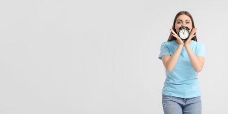 Young woman with alarm clock on light background
