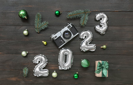 Figure 2023 made of balloons with photo camera, Christmas branches and balls on black wooden...