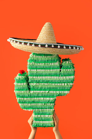 Woman holding Mexican pinata in shape of cactus with sombrero hat on color backgroundの写真素材