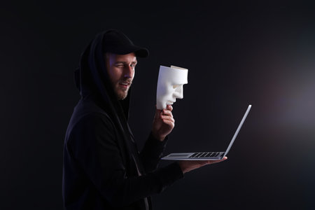 Hacker with laptop and mask on dark backgroundの写真素材