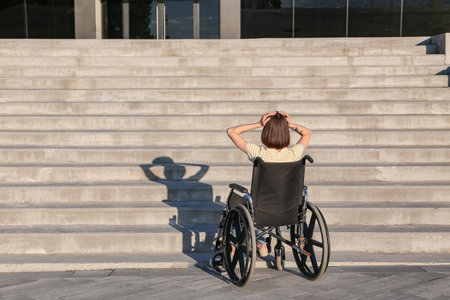 Stressed young woman in wheelchair near stairs outdoorsの写真素材