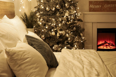 Big bed near glowing Christmas tree and fireplace in bedroom at nightの写真素材