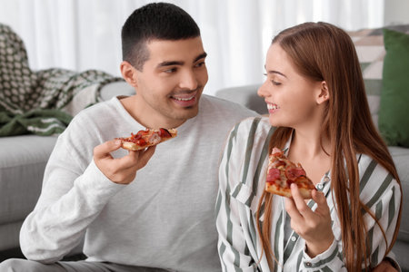 Happy young couple eating tasty pizza at homeの写真素材