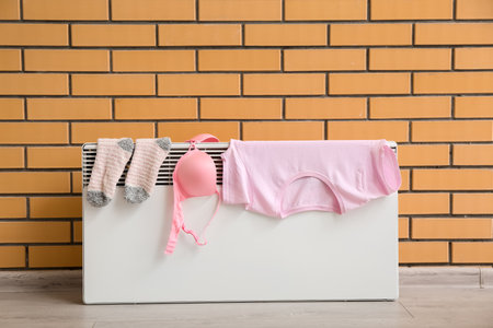 Female clothes drying on electric radiator near brick wallの写真素材