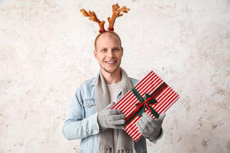 Handsome man in reindeer horns with Christmas present on light backgroundの写真素材