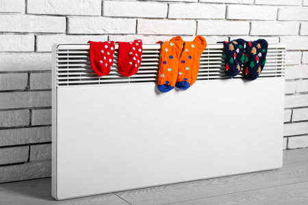Warm socks drying on electric radiator near white brick wallの写真素材